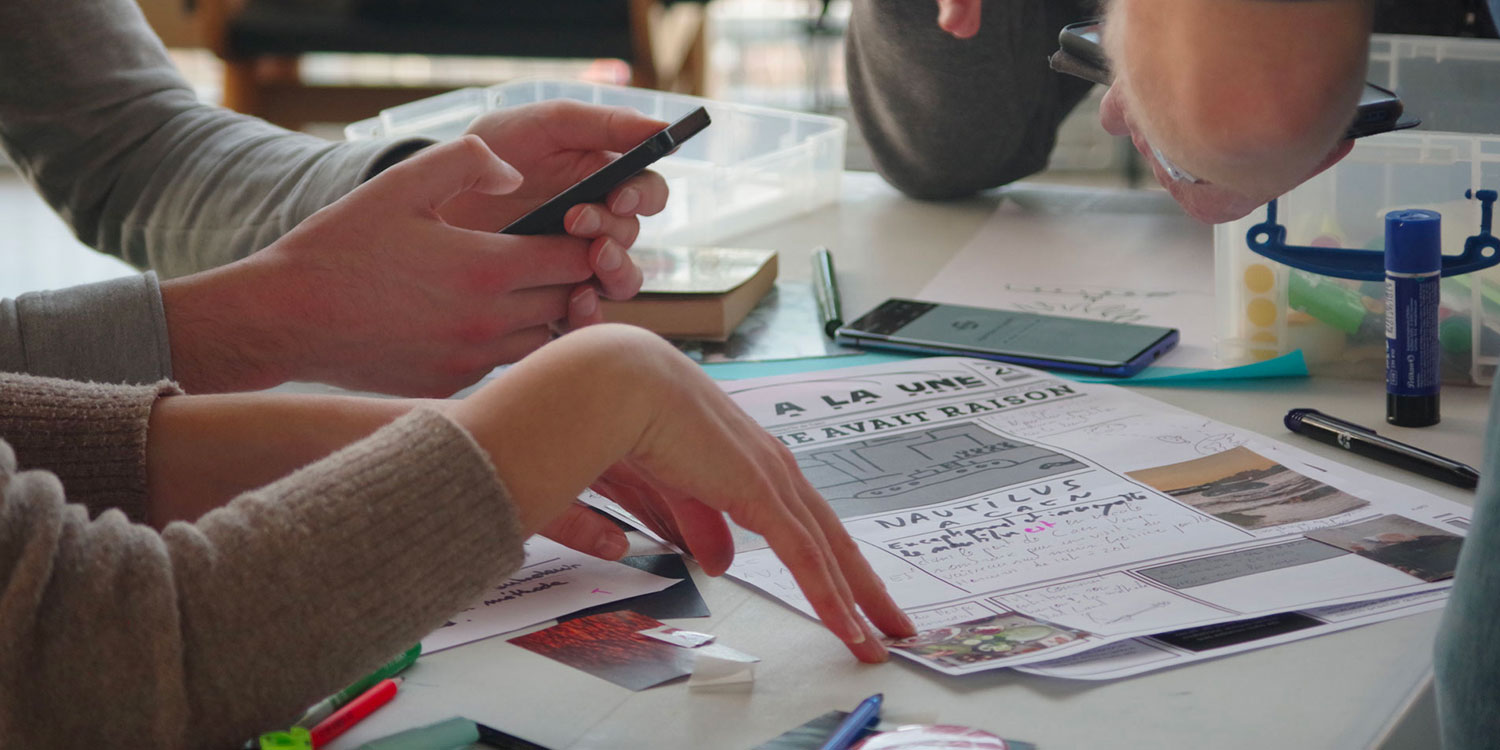 Les mains de personnes en train de manipuler un smartphone et des feuilles de papier au cours d'un atelier Papier connecté au Dôme à Caen.